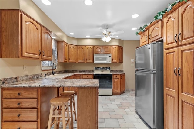 kitchen featuring ceiling fan, sink, kitchen peninsula, white appliances, and a breakfast bar