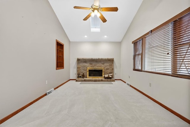 unfurnished living room featuring a fireplace, ceiling fan, vaulted ceiling with skylight, and carpet