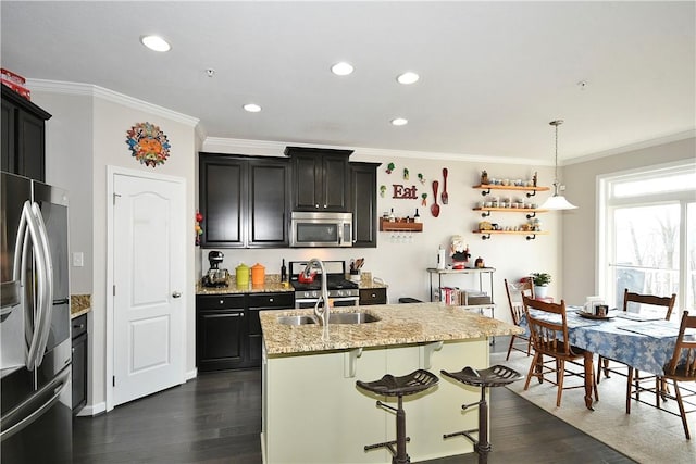 kitchen with light stone countertops, stainless steel appliances, dark wood-type flooring, pendant lighting, and an island with sink