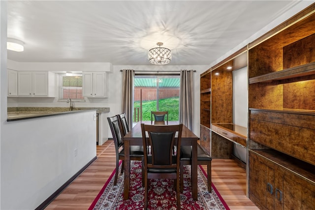 dining space featuring a healthy amount of sunlight, sink, light hardwood / wood-style floors, and an inviting chandelier