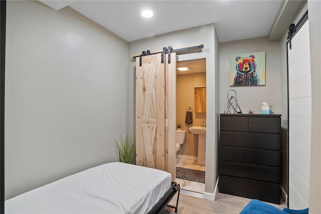 bedroom with ensuite bathroom, a barn door, light wood-type flooring, and sink