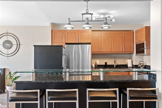 kitchen with stainless steel fridge, a kitchen breakfast bar, decorative light fixtures, dark stone countertops, and hardwood / wood-style floors