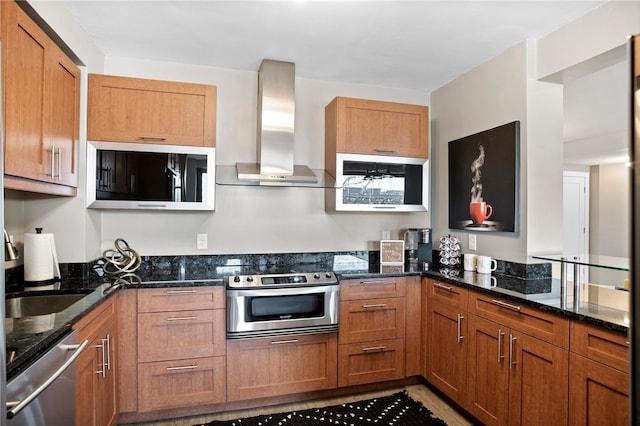 kitchen featuring kitchen peninsula, dark stone counters, wall chimney range hood, and appliances with stainless steel finishes