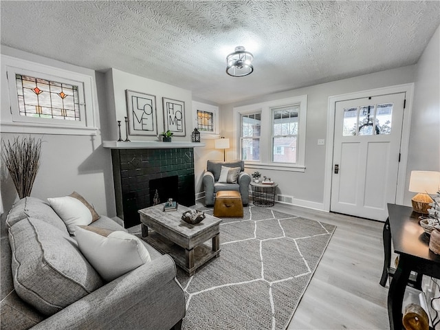 living room with a brick fireplace, a textured ceiling, and light wood-type flooring