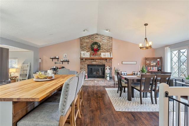 dining room featuring lofted ceiling, a chandelier, dark hardwood / wood-style floors, and a brick fireplace