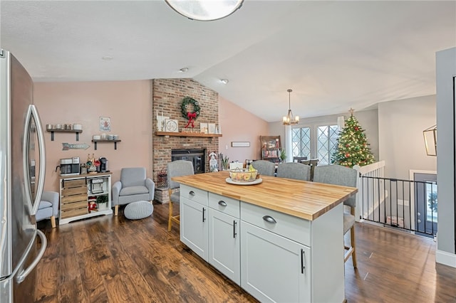 kitchen featuring wooden counters, a kitchen island, decorative light fixtures, white cabinetry, and stainless steel refrigerator