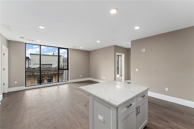 kitchen featuring hardwood / wood-style floors, white cabinets, expansive windows, light stone countertops, and a kitchen island