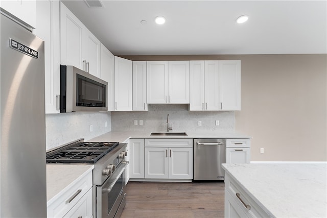 kitchen featuring hardwood / wood-style floors, sink, decorative backsplash, white cabinetry, and stainless steel appliances