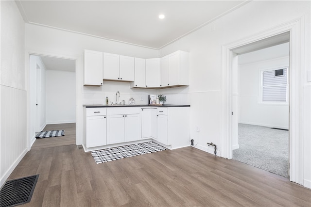 kitchen with white cabinets, light wood-type flooring, ornamental molding, and sink