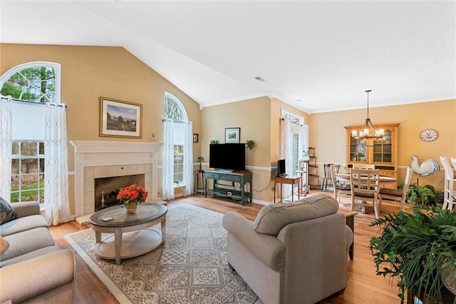 living room featuring an inviting chandelier, light hardwood / wood-style flooring, lofted ceiling, and a tiled fireplace