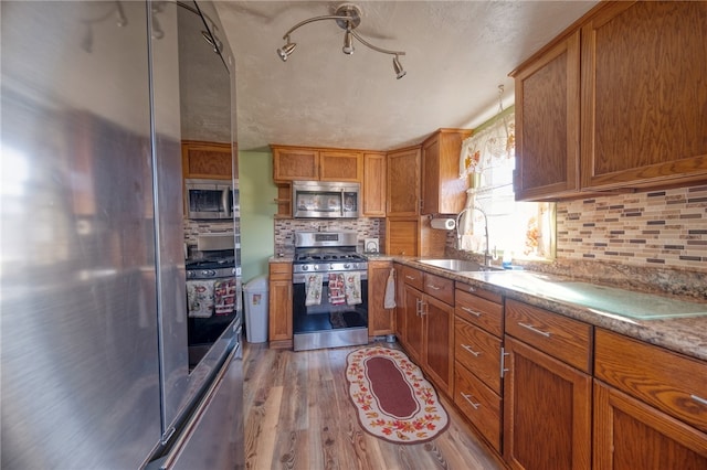 kitchen with sink, decorative backsplash, light stone countertops, appliances with stainless steel finishes, and wood-type flooring