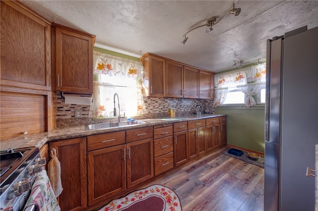 kitchen featuring light stone countertops, sink, stainless steel appliances, light hardwood / wood-style flooring, and backsplash