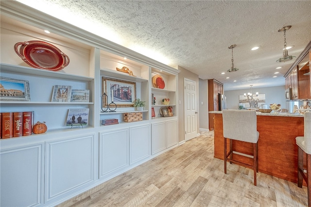 kitchen with a textured ceiling, an inviting chandelier, light hardwood / wood-style flooring, and stainless steel refrigerator