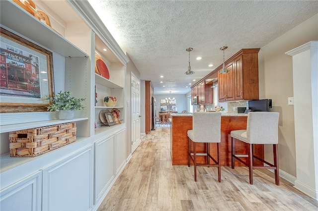 kitchen with hanging light fixtures, kitchen peninsula, a textured ceiling, a breakfast bar, and light wood-type flooring