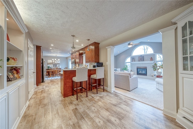 kitchen featuring lofted ceiling, ceiling fan with notable chandelier, light wood-type flooring, kitchen peninsula, and a breakfast bar area