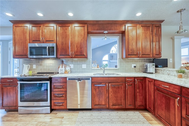 kitchen with sink, light hardwood / wood-style flooring, light stone countertops, appliances with stainless steel finishes, and decorative light fixtures