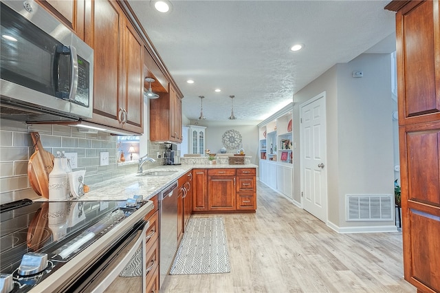 kitchen featuring sink, light hardwood / wood-style flooring, decorative backsplash, kitchen peninsula, and stainless steel appliances