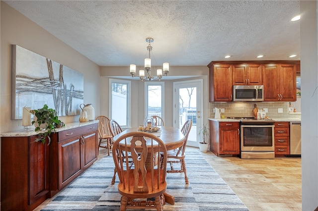 kitchen with stainless steel appliances, tasteful backsplash, a chandelier, pendant lighting, and light wood-type flooring