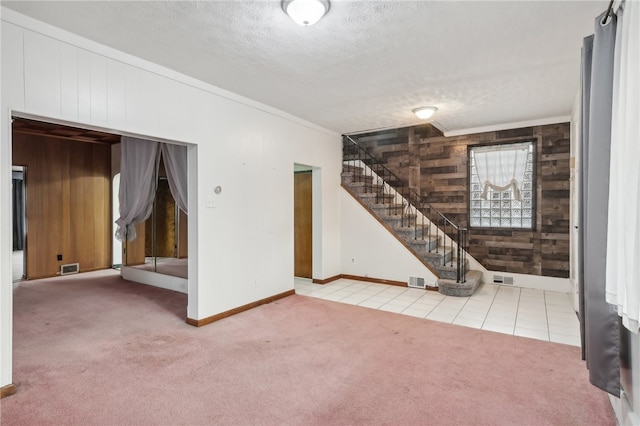 interior space with a textured ceiling, light colored carpet, ornamental molding, and wood walls