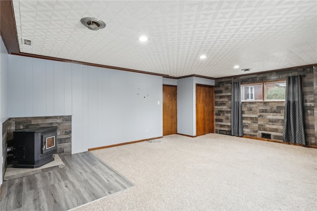 unfurnished living room featuring a wood stove, ornamental molding, and wood walls