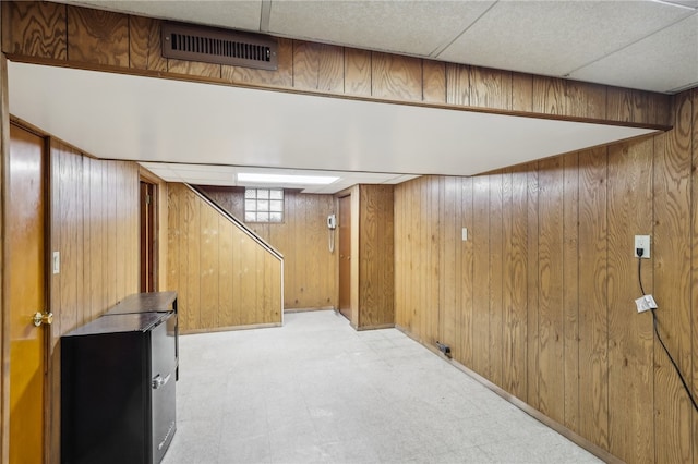 basement with a paneled ceiling and wood walls