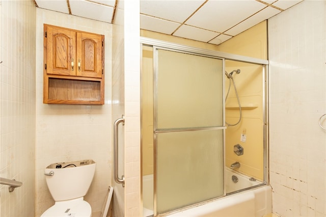 bathroom featuring toilet, a drop ceiling, and bath / shower combo with glass door