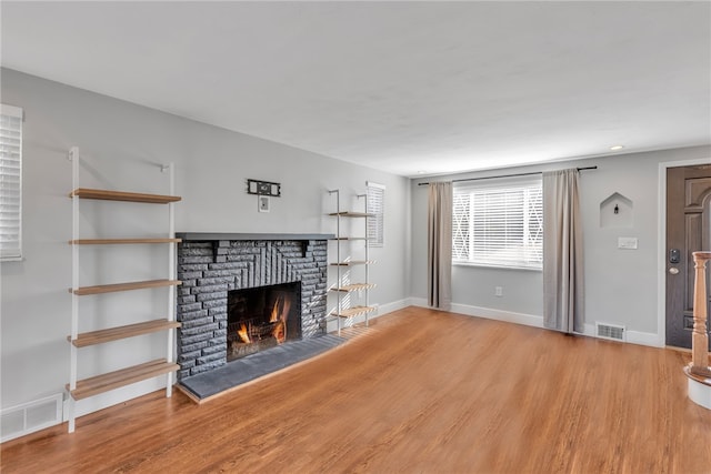 unfurnished living room with wood-type flooring and a brick fireplace