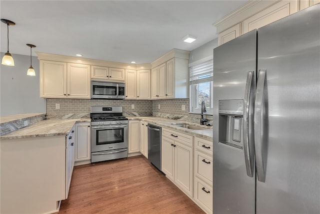 kitchen featuring pendant lighting, backsplash, sink, light hardwood / wood-style flooring, and appliances with stainless steel finishes