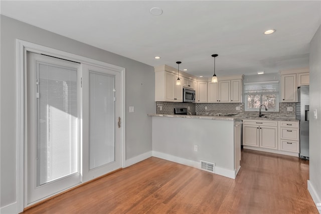 kitchen with kitchen peninsula, stainless steel appliances, decorative light fixtures, hardwood / wood-style flooring, and white cabinets