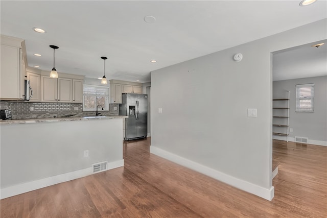 kitchen with light stone countertops, sink, hanging light fixtures, stainless steel appliances, and hardwood / wood-style flooring