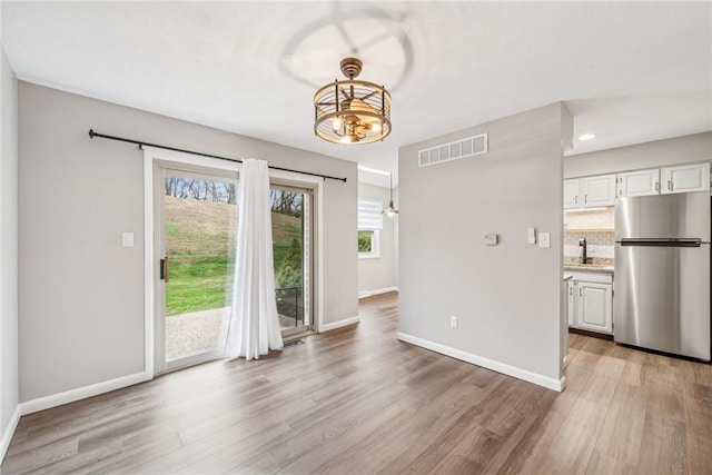 unfurnished dining area with a notable chandelier, sink, and light hardwood / wood-style flooring