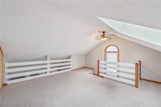 additional living space featuring carpet flooring, a textured ceiling, ceiling fan, and vaulted ceiling with skylight