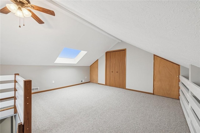 bonus room with ceiling fan, vaulted ceiling with skylight, light colored carpet, and a textured ceiling