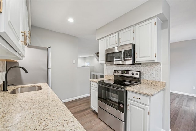 kitchen featuring light stone counters, stainless steel appliances, sink, wood-type flooring, and white cabinetry