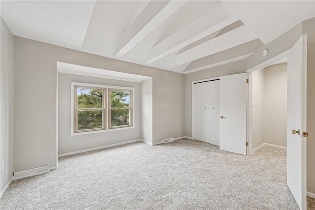 unfurnished bedroom featuring beamed ceiling, light colored carpet, and a closet