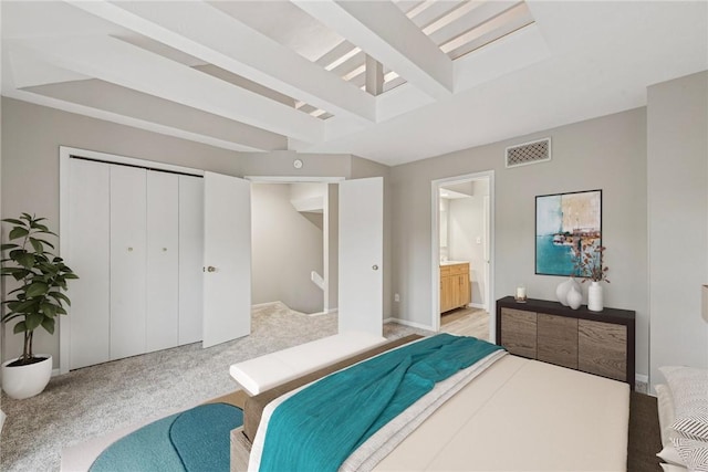 carpeted bedroom with beam ceiling, ensuite bathroom, and a closet