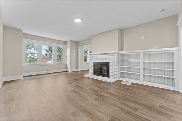 unfurnished living room featuring wood-type flooring and a brick fireplace