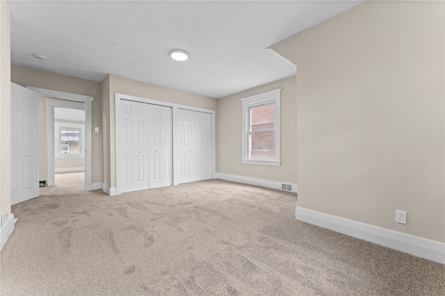 unfurnished bedroom featuring two closets, light colored carpet, and multiple windows