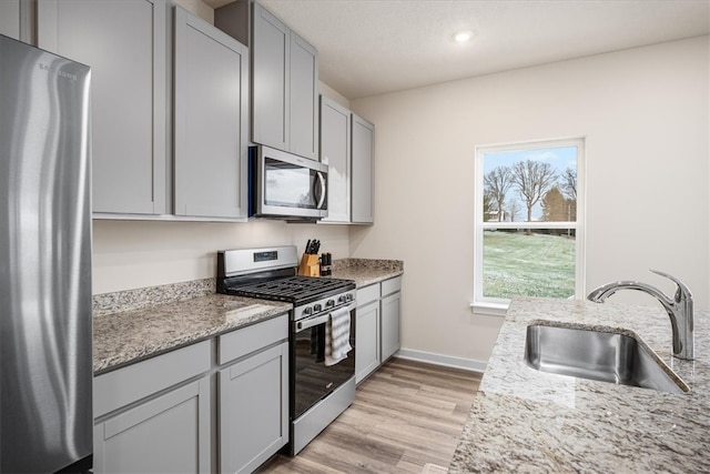 kitchen with light stone countertops, sink, light wood-type flooring, and appliances with stainless steel finishes