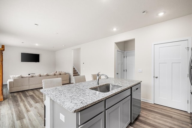 kitchen featuring light stone countertops, sink, a center island with sink, dishwasher, and light hardwood / wood-style floors