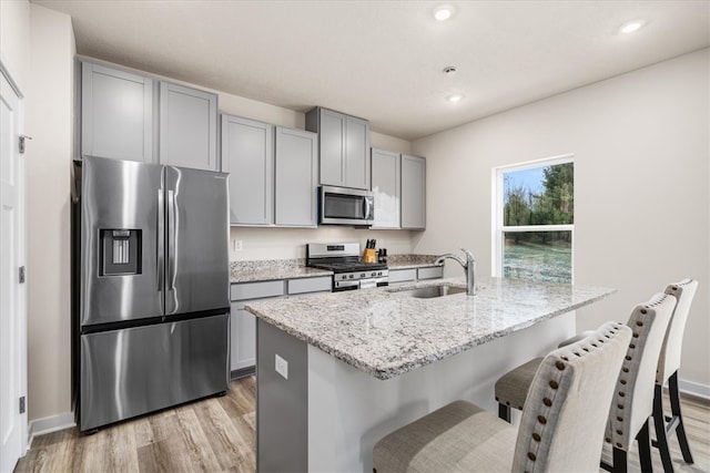 kitchen featuring a kitchen island with sink, light hardwood / wood-style flooring, light stone countertops, and appliances with stainless steel finishes