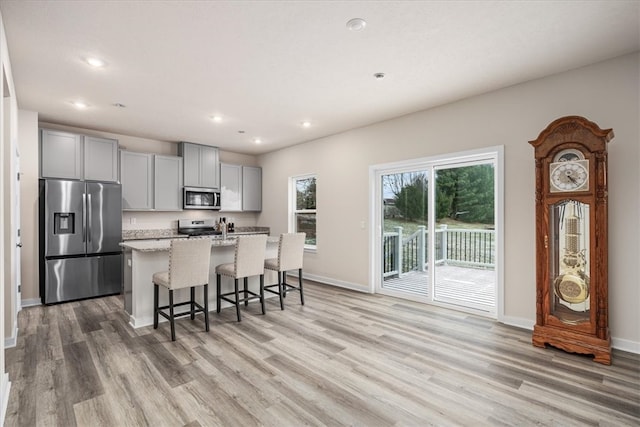 kitchen featuring light stone counters, light hardwood / wood-style floors, stainless steel appliances, gray cabinets, and an island with sink