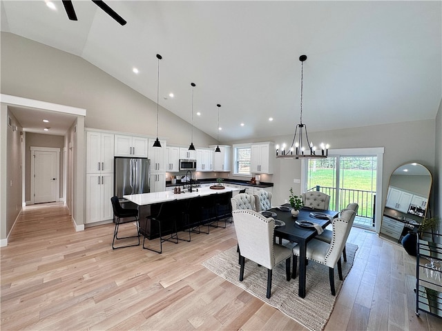 dining room with ceiling fan with notable chandelier, light hardwood / wood-style floors, sink, and high vaulted ceiling