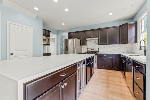 kitchen featuring appliances with stainless steel finishes, backsplash, sink, light hardwood / wood-style flooring, and a center island