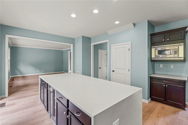 kitchen featuring ornamental molding, dark brown cabinets, light hardwood / wood-style floors, a kitchen island, and stainless steel microwave