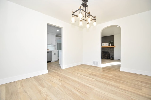 spare room featuring a stone fireplace, light hardwood / wood-style flooring, and a notable chandelier