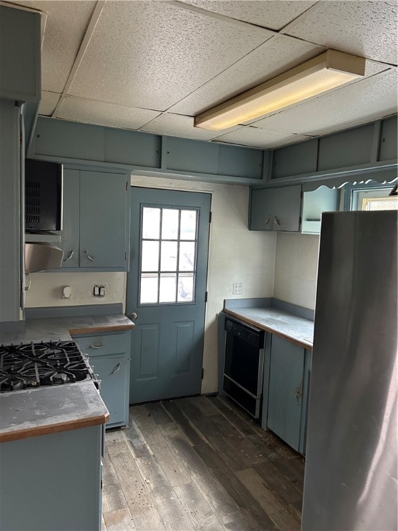 kitchen featuring stainless steel refrigerator, a drop ceiling, dark wood-type flooring, black dishwasher, and range