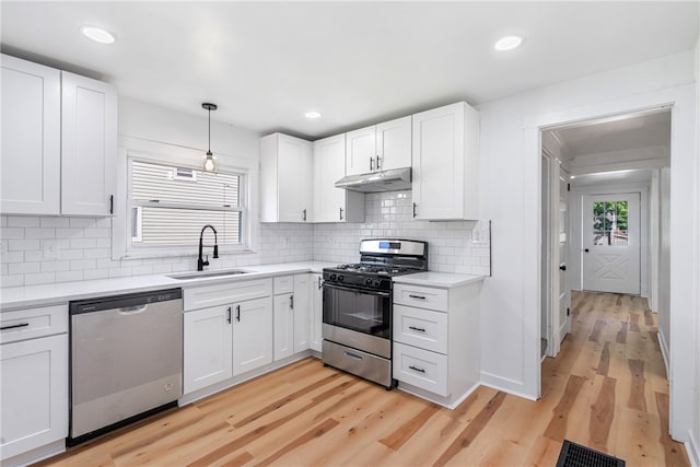 kitchen with stainless steel appliances, sink, decorative light fixtures, white cabinets, and light hardwood / wood-style floors