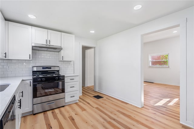 kitchen with white cabinets, light stone countertops, tasteful backsplash, light hardwood / wood-style floors, and stainless steel appliances