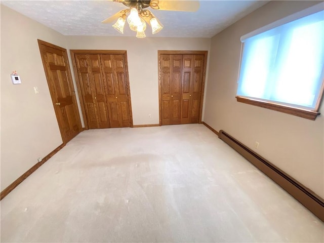 unfurnished bedroom with carpet flooring, a baseboard radiator, ceiling fan, and multiple closets